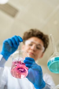 Below view of chemist in protective gloves stirring reagents into beaker while preparing for experiment